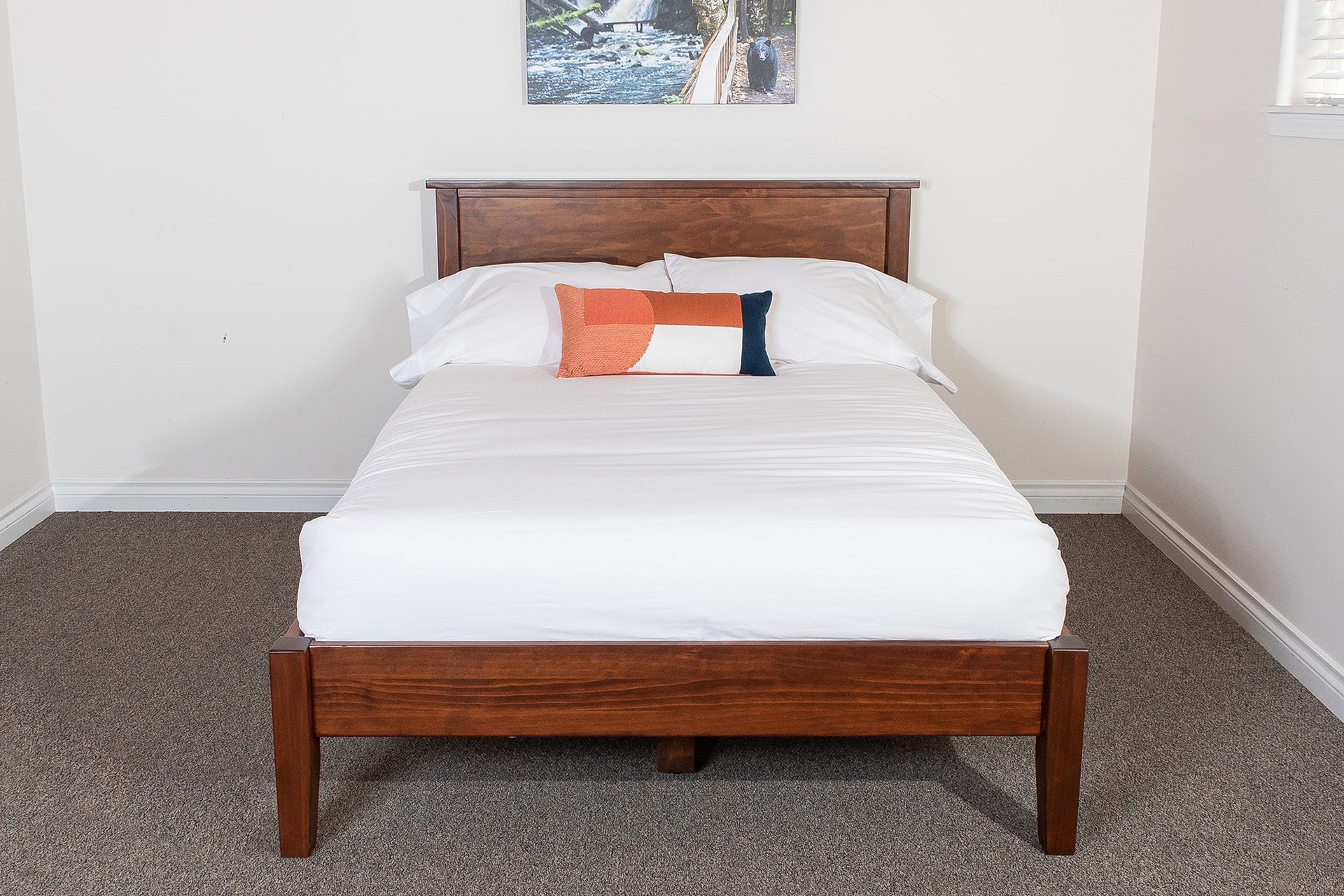 A solid wood platform bed frame with a headboard, displayed in a room with a white mattress and bedding, in a brown stain finish.